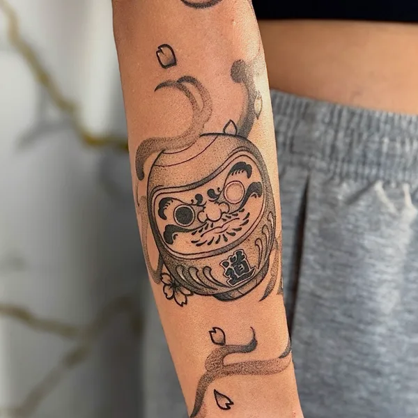 Daruma japonés con flor y pétalos de cerezo en el antebrazo