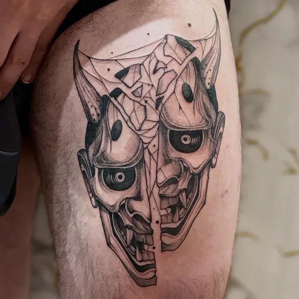 Máscara hannya partida en dos, en negro, en un muslo